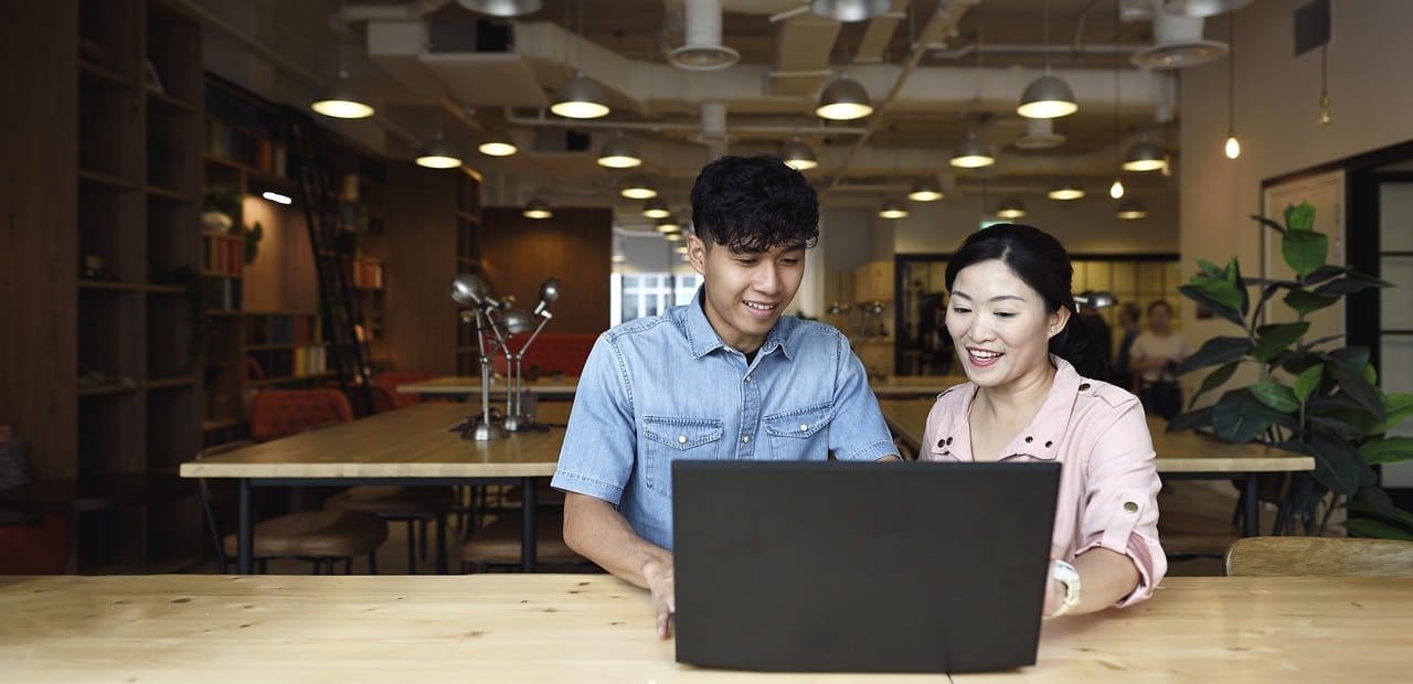 Parent and child sitting together at a laptop in a modern workspace, reviewing financial basics and discussing foundational investing concepts.