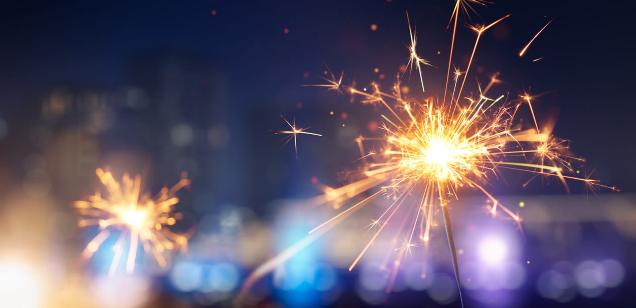 Close-up of sparklers glowing brightly against a blurred cityscape at night.