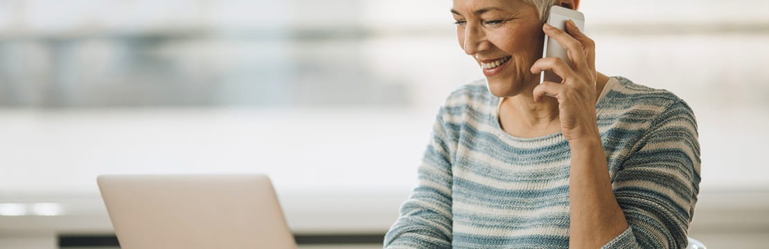 Person working at a laptop while talking on a mobile phone, with a coffee mug on the table.