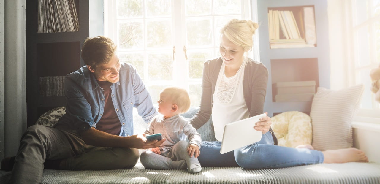 A young family sits together by a bright window, using a tablet and smartphone while discussing tax planning.