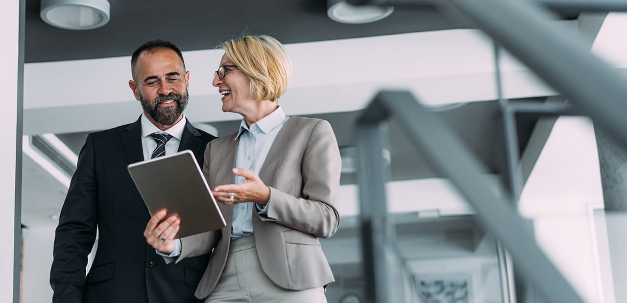 An advisor and client smiling, looking at tablet while walking