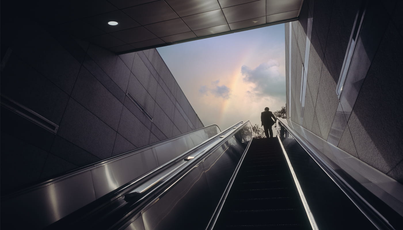 Person ascending an escalator toward daylight, symbolizing 2026 tax law changes limiting high earners’ pre-tax catch-up retirement contributions.